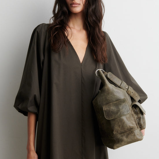 Woman wearing a dark green dress holding a matching backpack against a white background from Second Female