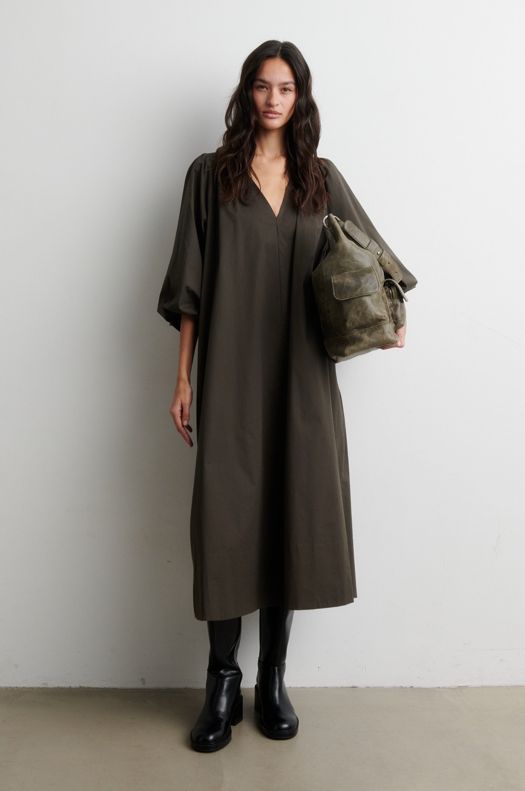Woman wearing a long olive green dress holding a matching bag against a white background from Second Female