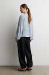 Woman wearing a light blue shirt and black pants against a white wall from Second Female