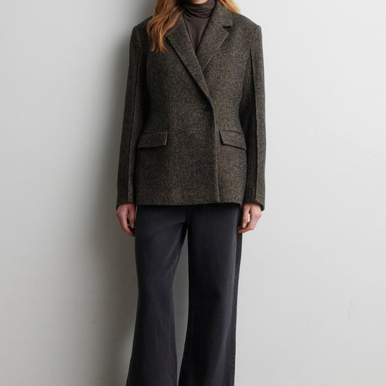 Woman wearing a gray blazer and black pants against a white wall