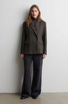 Woman wearing a gray blazer and black pants against a white wall