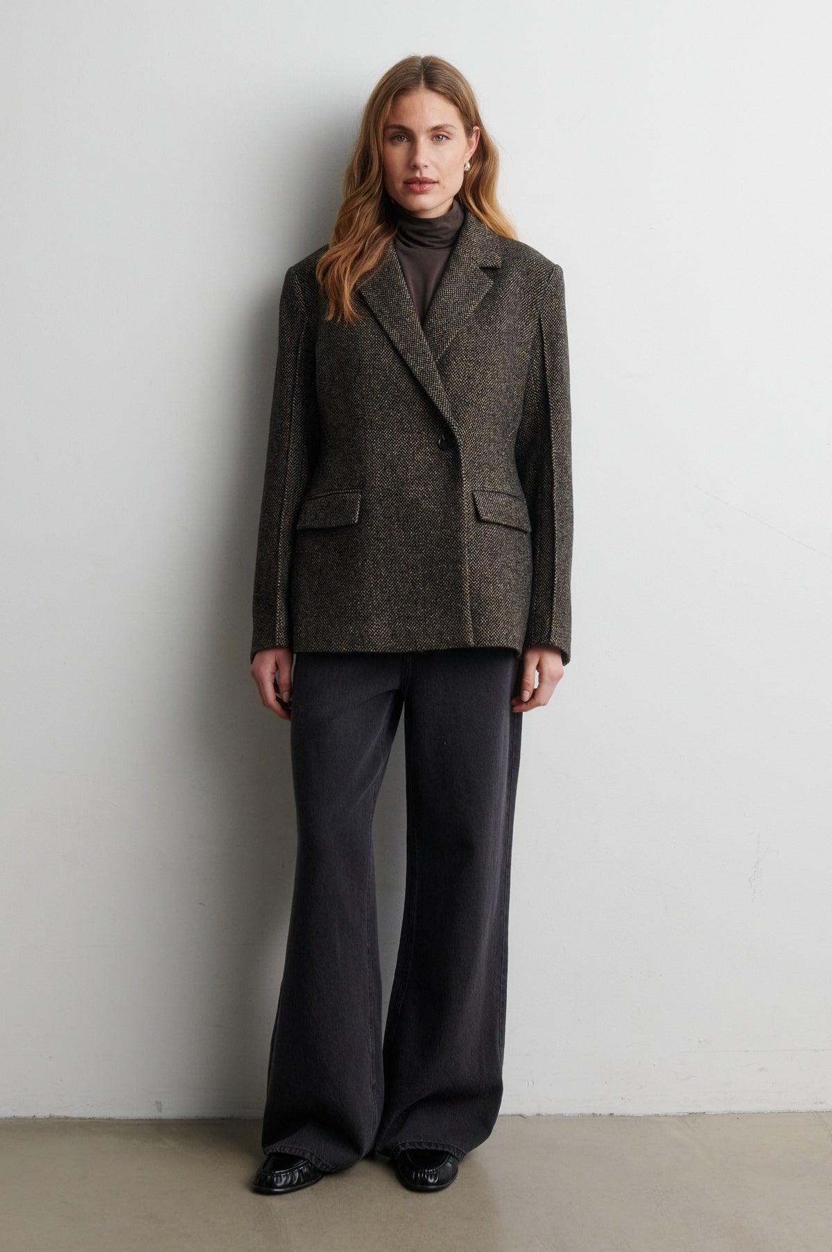 Woman wearing a gray blazer and black pants against a white wall