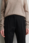 Person wearing a beige sweater and black trousers against a neutral background from Second Female