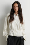 model wearing a cream satin button up shirt with black trousers on a plain white background
