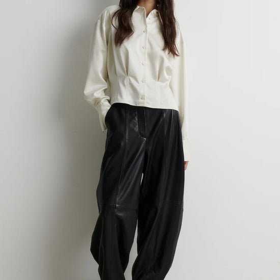 full body shot of a model wearing a short button up satin shirt and leather black trousers and boots 