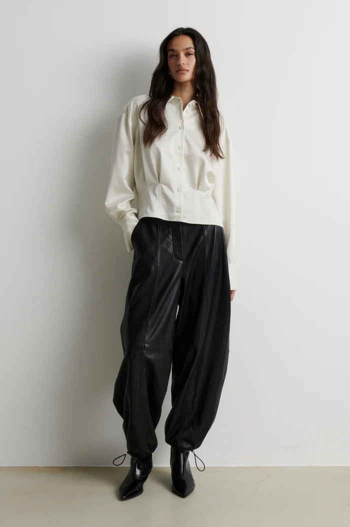 full body shot of a model wearing a short button up satin shirt and leather black trousers and boots 