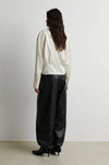 A model shown from the back wearing a cream-colored long-sleeve top and black wide-leg pants, standing against a plain light gray wall.