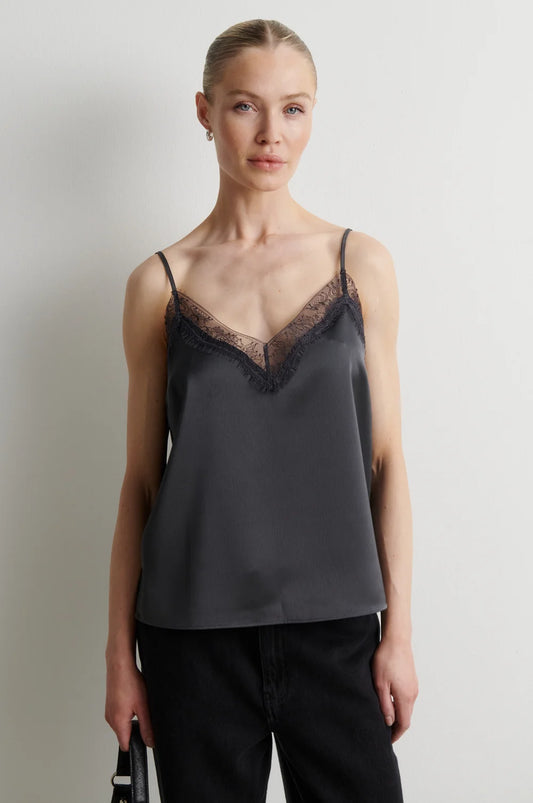A woman modeling a dark gray satin camisole top with black lace trim along the V-neckline, paired with black pants, against a plain light gray background.