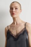 A woman wearing a dark gray satin camisole with black lace trim and thin spaghetti straps, photographed against a neutral light gray background.