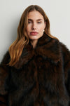Woman wearing a dark brown fur coat against a plain background rom Second Female