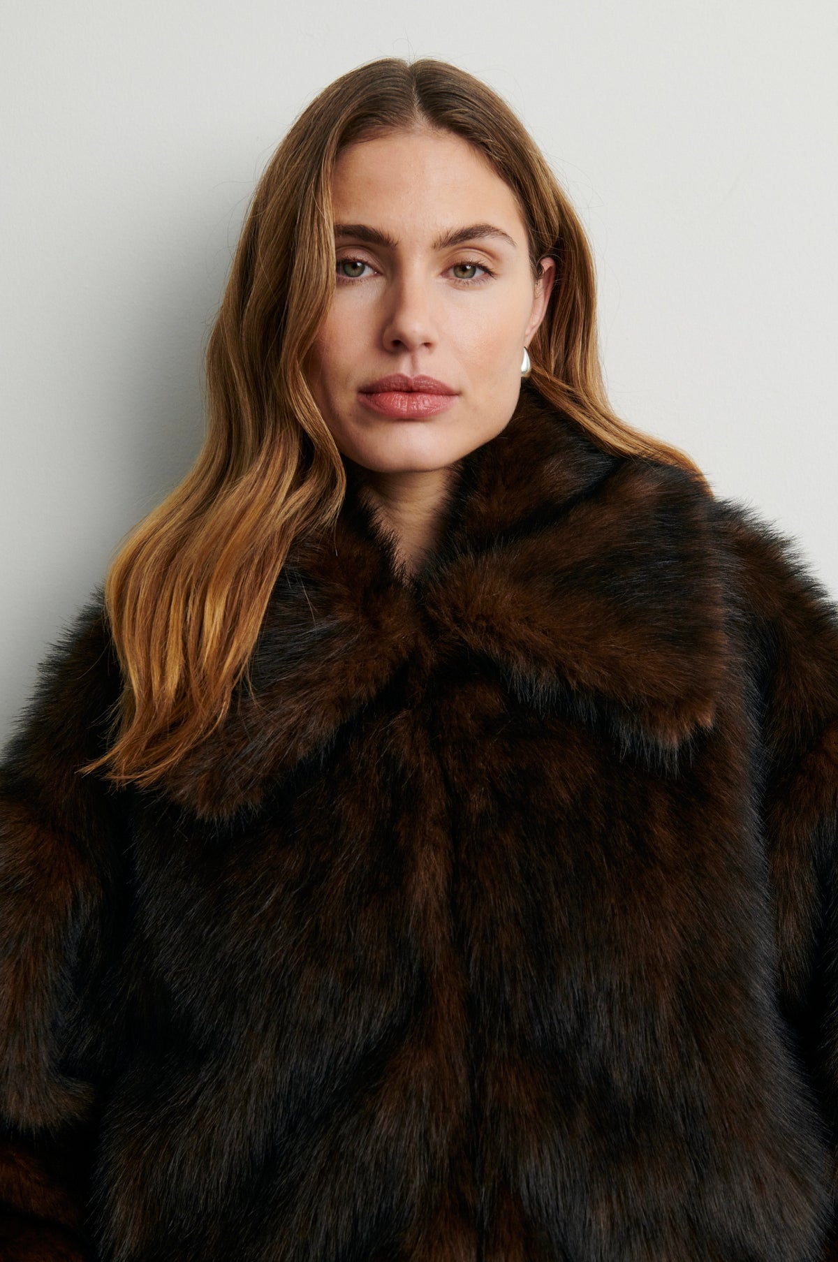 Woman wearing a dark brown fur coat against a plain background rom Second Female