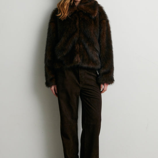 Woman wearing a dark brown fur coat and pants against a white wall from Second Female