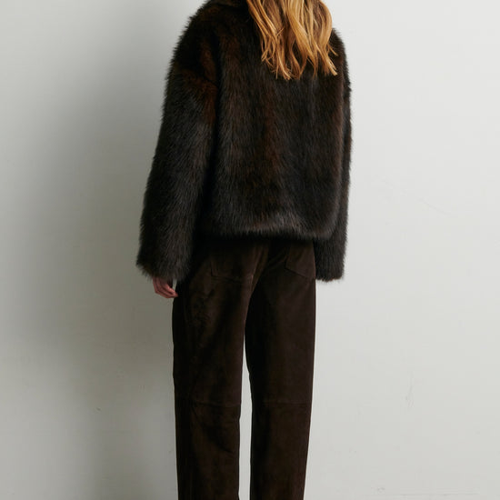 Rear view of Person wearing a dark fur coat and brown pants against a white from Second Female 