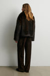 Rear view of Person wearing a dark fur coat and brown pants against a white from Second Female 