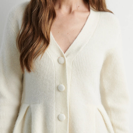 A close-up of a woman wearing a cream-colored, ribbed knit cardigan with a V-neck and large white buttons.