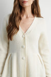 A close-up of a woman wearing a cream-colored, ribbed knit cardigan with a V-neck and large white buttons.