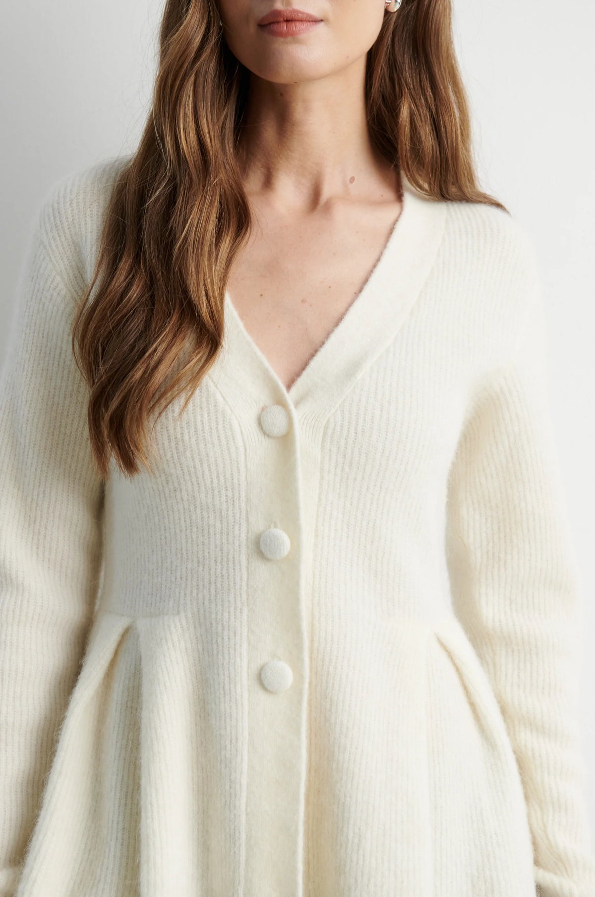 A close-up of a woman wearing a cream-colored, ribbed knit cardigan with a V-neck and large white buttons.