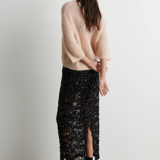 Rear view of short sleeve oipen weave pale pink knit worn with black sequin skirt