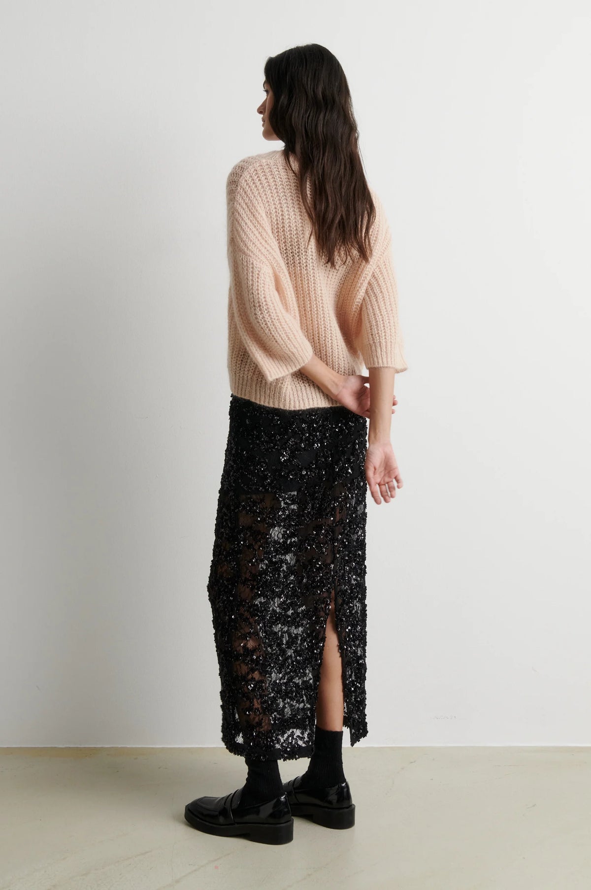 Rear view of short sleeve oipen weave pale pink knit worn with black sequin skirt