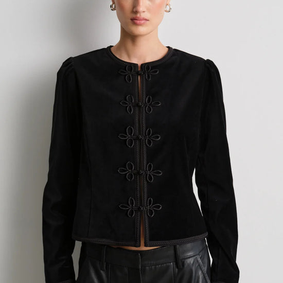 model wearing black leather trousers and a black velvet nepoleon style jacket with a plain background