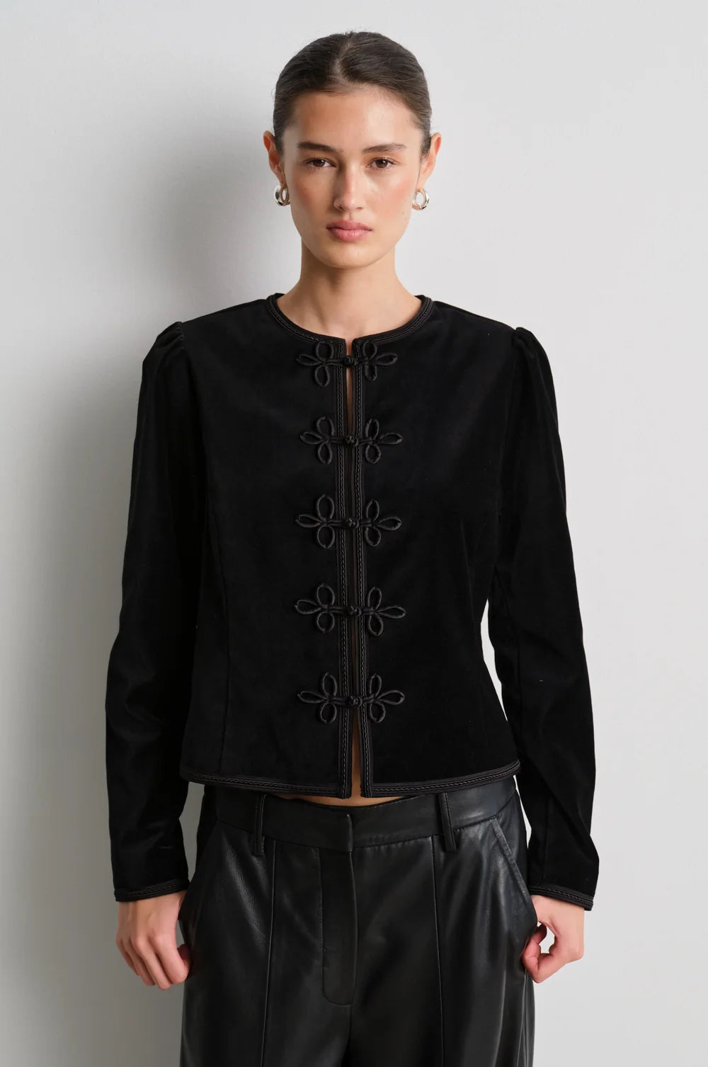 model wearing black leather trousers and a black velvet nepoleon style jacket with a plain background