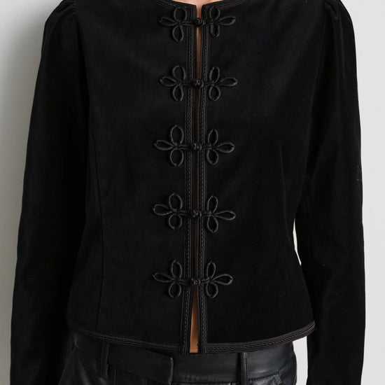 model wearing black leather trousers and a black velvet nepoleon style jacket with a plain background