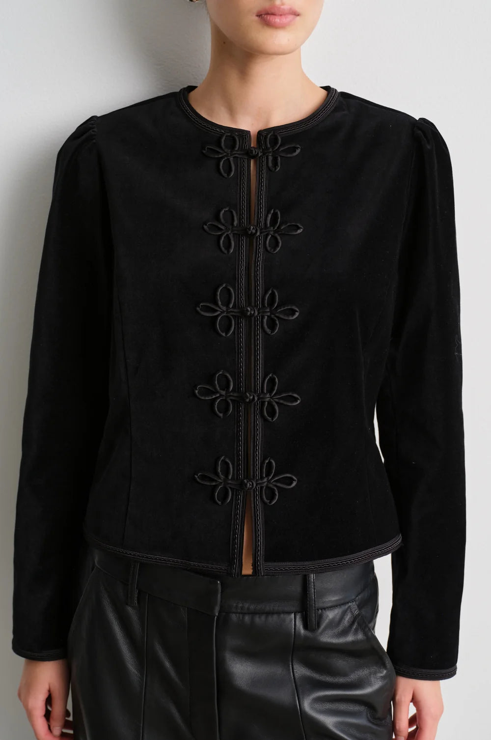 model wearing black leather trousers and a black velvet nepoleon style jacket with a plain background
