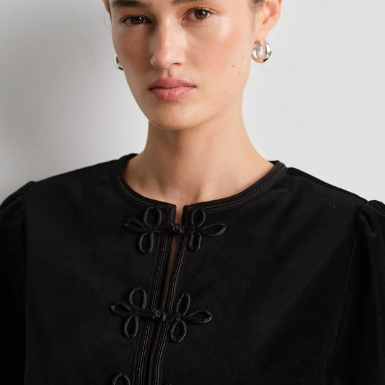 model wearing black leather trousers and a black velvet nepoleon style jacket with a plain background