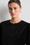model wearing black leather trousers and a black velvet nepoleon style jacket with a plain background