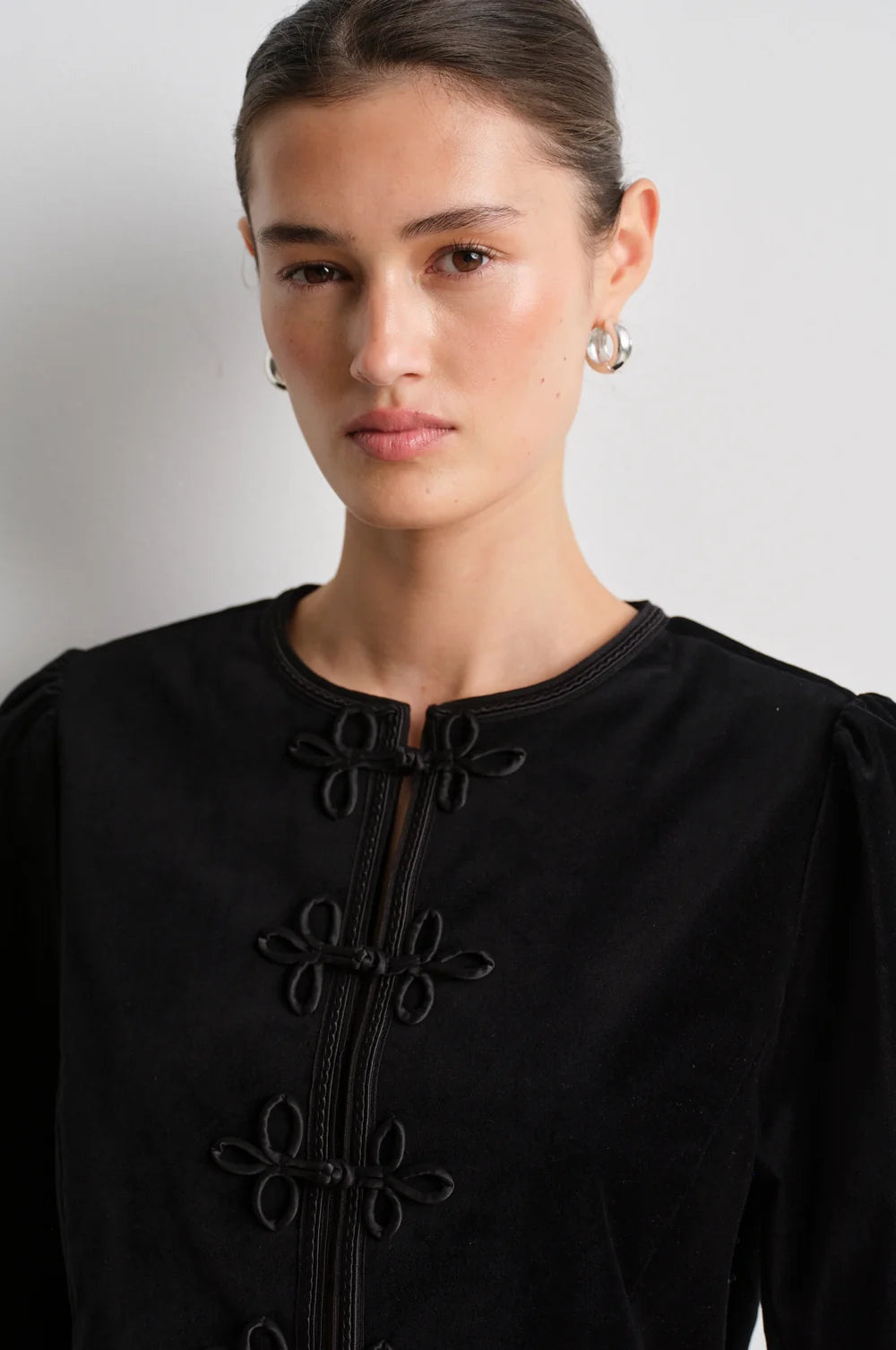 model wearing black leather trousers and a black velvet nepoleon style jacket with a plain background