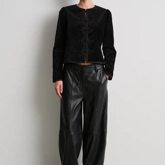 model wearing black leather trousers and a black velvet nepoleon style jacket with a plain background