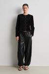 model wearing black leather trousers and a black velvet nepoleon style jacket with a plain background