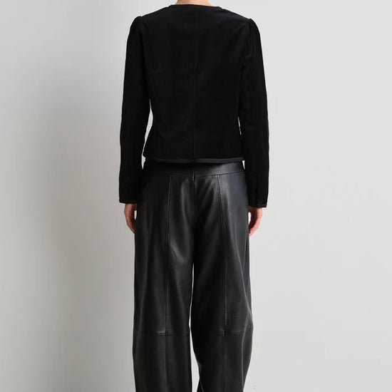 model wearing black leather trousers and a black velvet nepoleon style jacket with a plain background