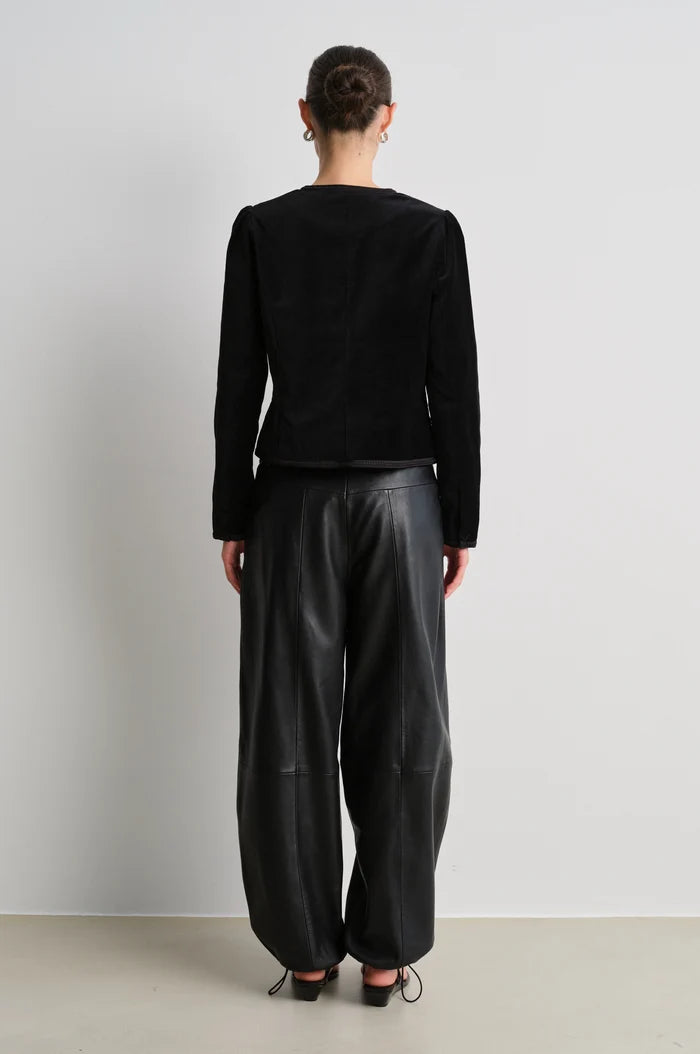 model wearing black leather trousers and a black velvet nepoleon style jacket with a plain background
