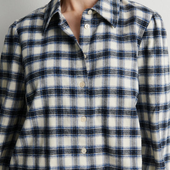 A close-up of a person wearing a long-sleeve button-front plaid shirt in off-white with navy and thin gray stripes.