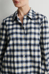 A close-up of a person wearing a long-sleeve button-front plaid shirt in off-white with navy and thin gray stripes.