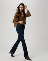 A woman modeling a brown and gold patterned blouse with bell sleeves, dark blue jeans, and dark brown heeled ankle boots, carrying a brown bag against a light gray studio background.