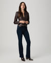 A woman modeling a dark brown satin long-sleeve blouse tucked into dark blue flare jeans with dark brown heeled ankle boots, photographed against a light gray studio background.