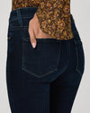 Close-up back view of a person wearing dark indigo denim jeans with a floral-patterned blouse tucked into the waistband, against a light gray studio background.