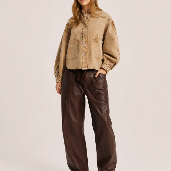 A woman modeling a cropped tan suede-like button-up jacket with voluminous sleeves, paired with dark brown wide-leg faux-leather pants and black pointed boots, against a plain light beige studio background.