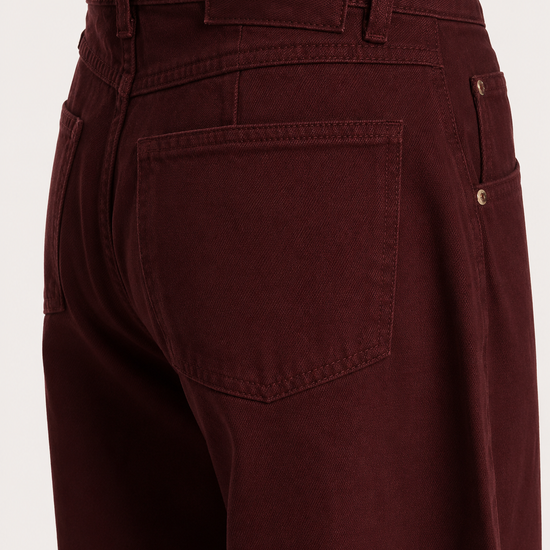 Close-up of the back waistband and rear pocket area of dark burgundy denim jeans, showing the brand label 'ESSENTIEL ANTWERP' and a button closure.