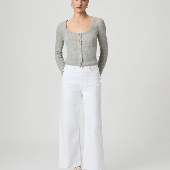 Woman wearing a gray cardigan and white paige jeans on a plain background