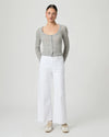 Woman wearing a gray cardigan and white paige jeans on a plain background