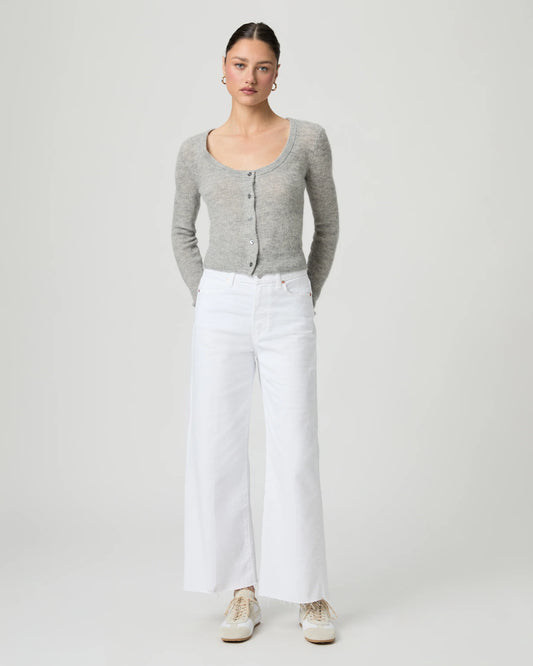 Woman wearing a gray cardigan and white paige jeans on a plain background