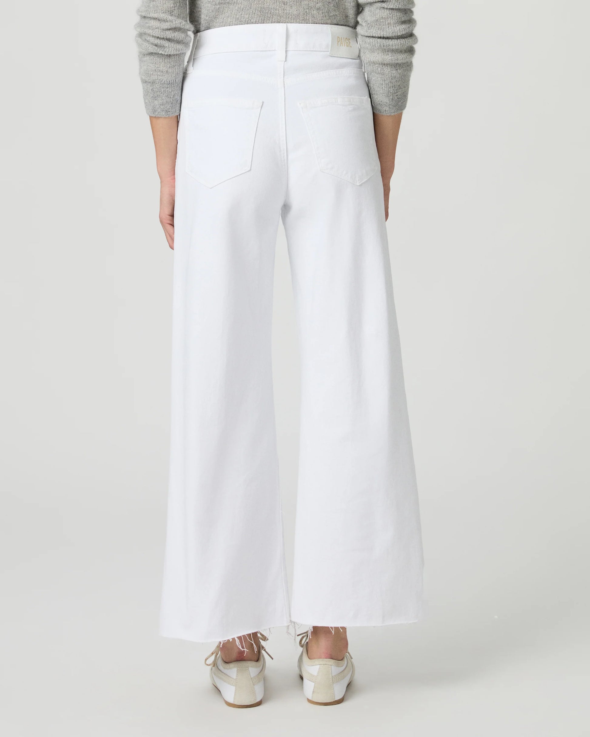 Person wearing white wide-leg paige jeans on a plain background rear view