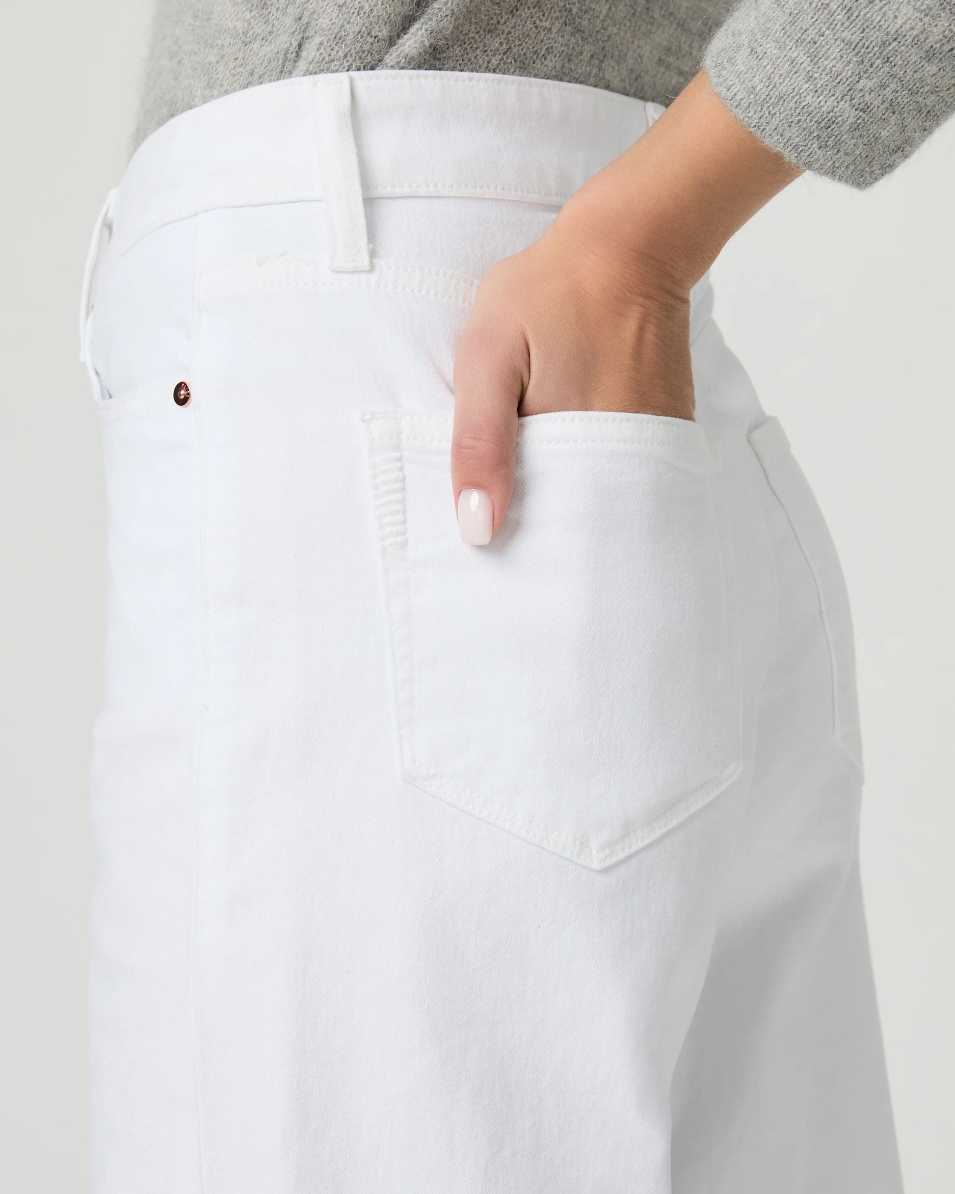 Person wearing white wide-leg paige jeans on a plain background close up