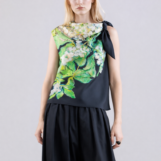 Woman wearing a silk sleeveless top with floral design and black pants on a light gray background