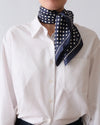 Person wearing a navy blue scarf with white polka dots over a white shirt against a plain background