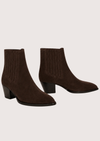 A pair of dark brown suede ankle boots with ribbed elastic side panels and low block heels, displayed against a solid light beige background.