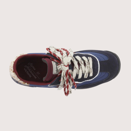 A low-top fashion sneaker, featuring navy blue suede and mesh panels, burgundy accents, patterned white and burgundy laces, and a cream midsole, shown against a plain light gray background.